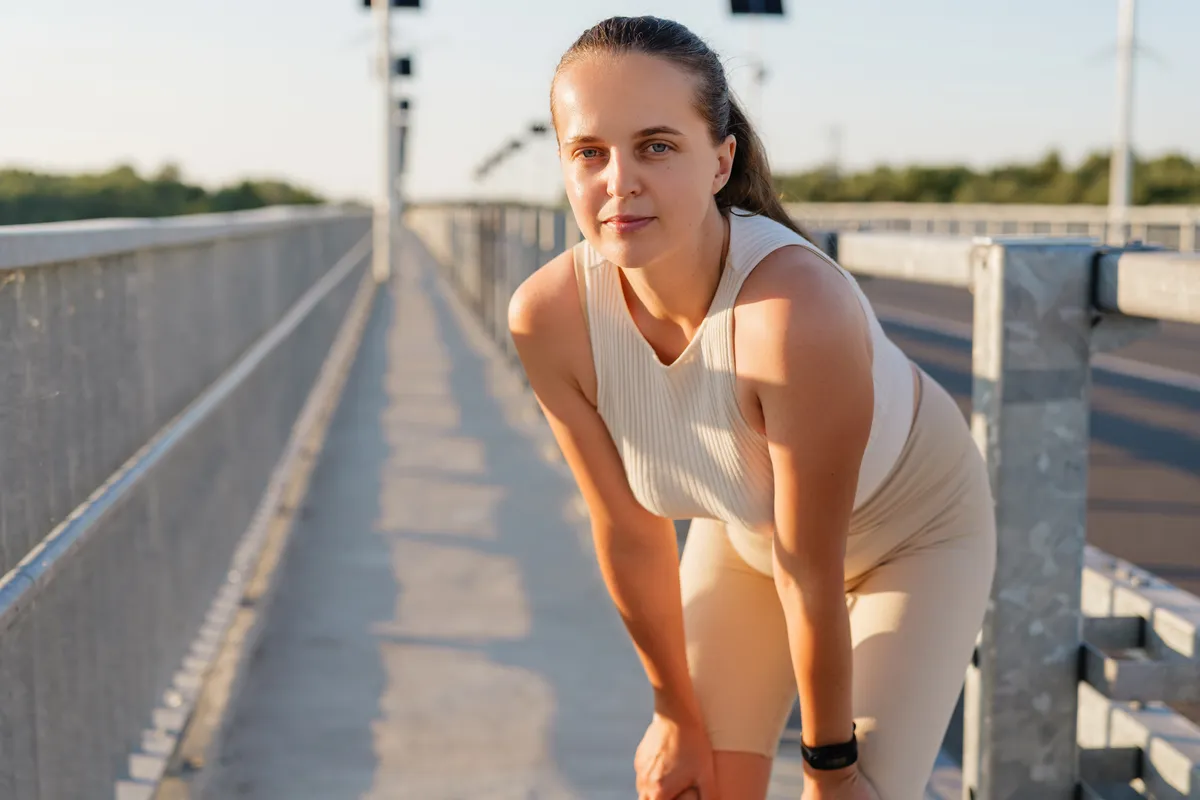 A woman in athletic wear with a smartwatch taking a break during an outdoor workout